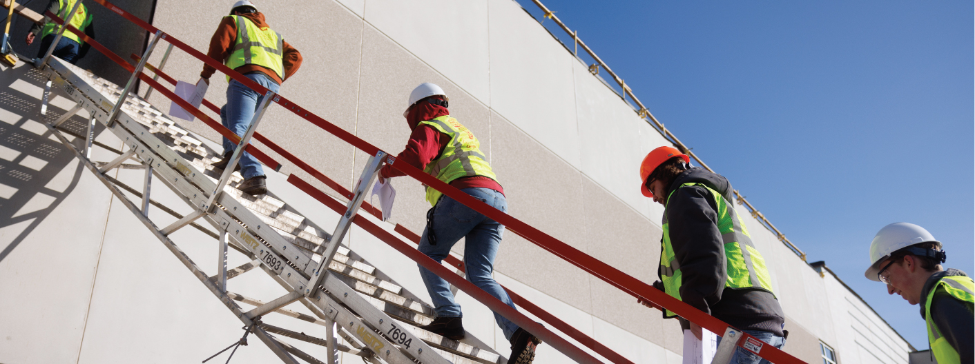 Students walking up a ladder in hard hats and reflective vests.