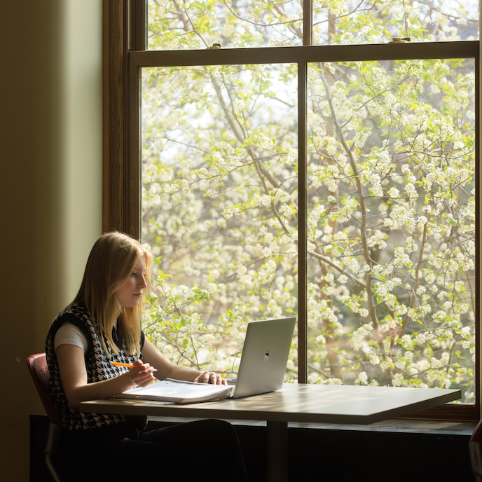 A student studies on a laptop sitting next to a window in Marston Hall.